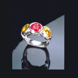 Three-stone ring wrapping platinum ribbons around a hot Pink and Yellow Sapphire suite.