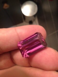 Pink step cut tourmaline positioned between someone's fingers