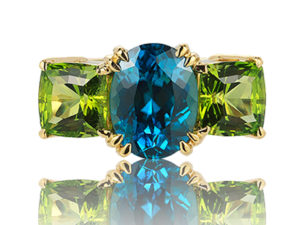 “Heaven & Earth” three-stone ring in 18 karat yellow gold featuring a 5.49 carats vivid Blue Zircon combined with a 4.22 carats pair of Peridot.