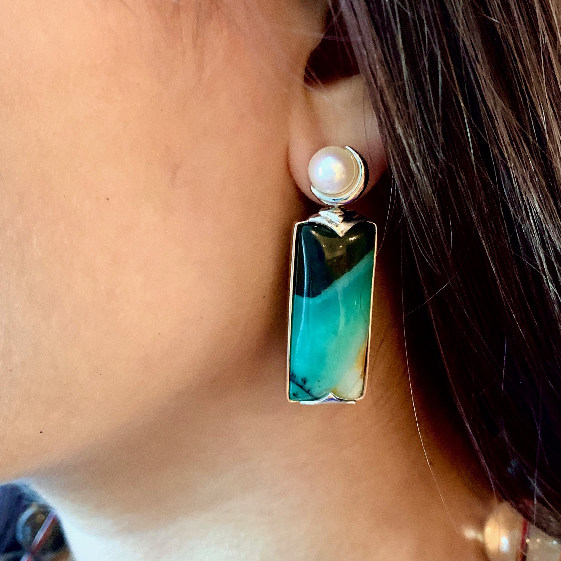 Close-up of model wearing opalized earrings in deep ocean green and aqua green topped with a round white pearl