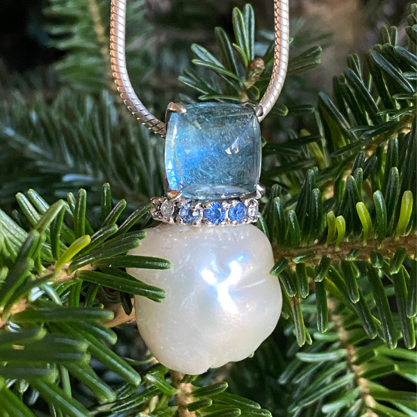 Pearl, aquamarine, diamond and sapphire pendant with evergreen tree background