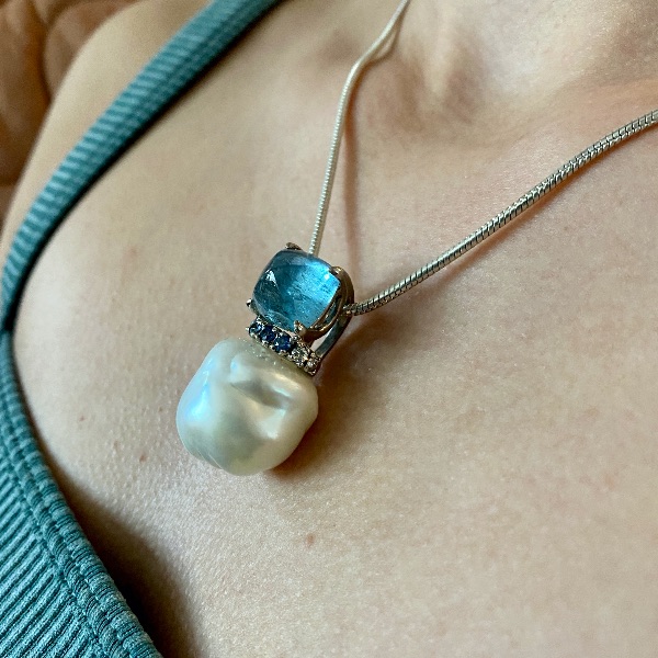 Pearl, aquamarine, diamond and sapphire pendant worn by woman with blue top