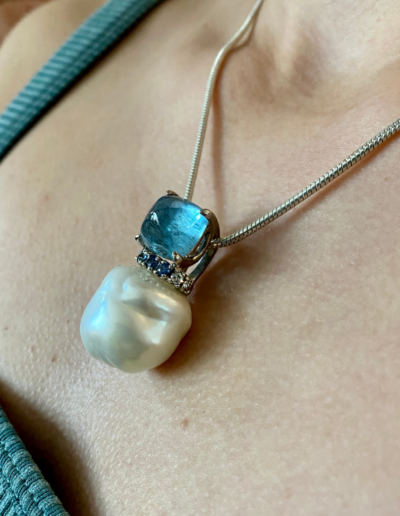 18 karat white gold pendant featuring 20x21 mm Baroque Pearl, 9.31 carat Aquamarine sugarloaf cabochon, and Blue Sapphire and Diamond accent.