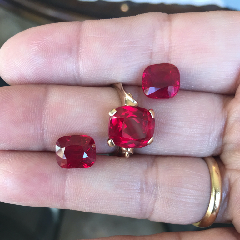Two loose rubies and a ruby ring are held in hand